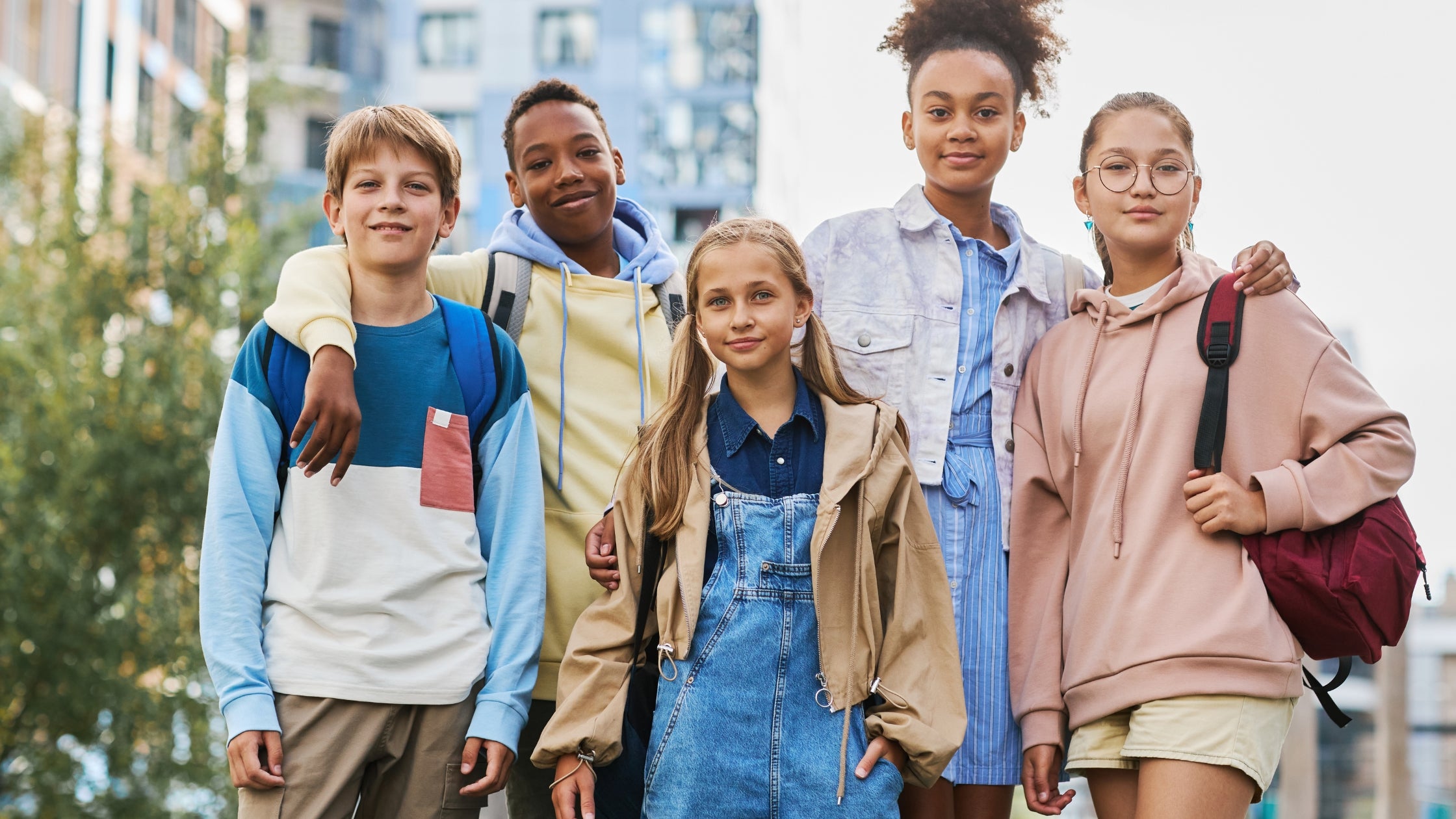 Group of smiling tweens and teens with school bags outside a school